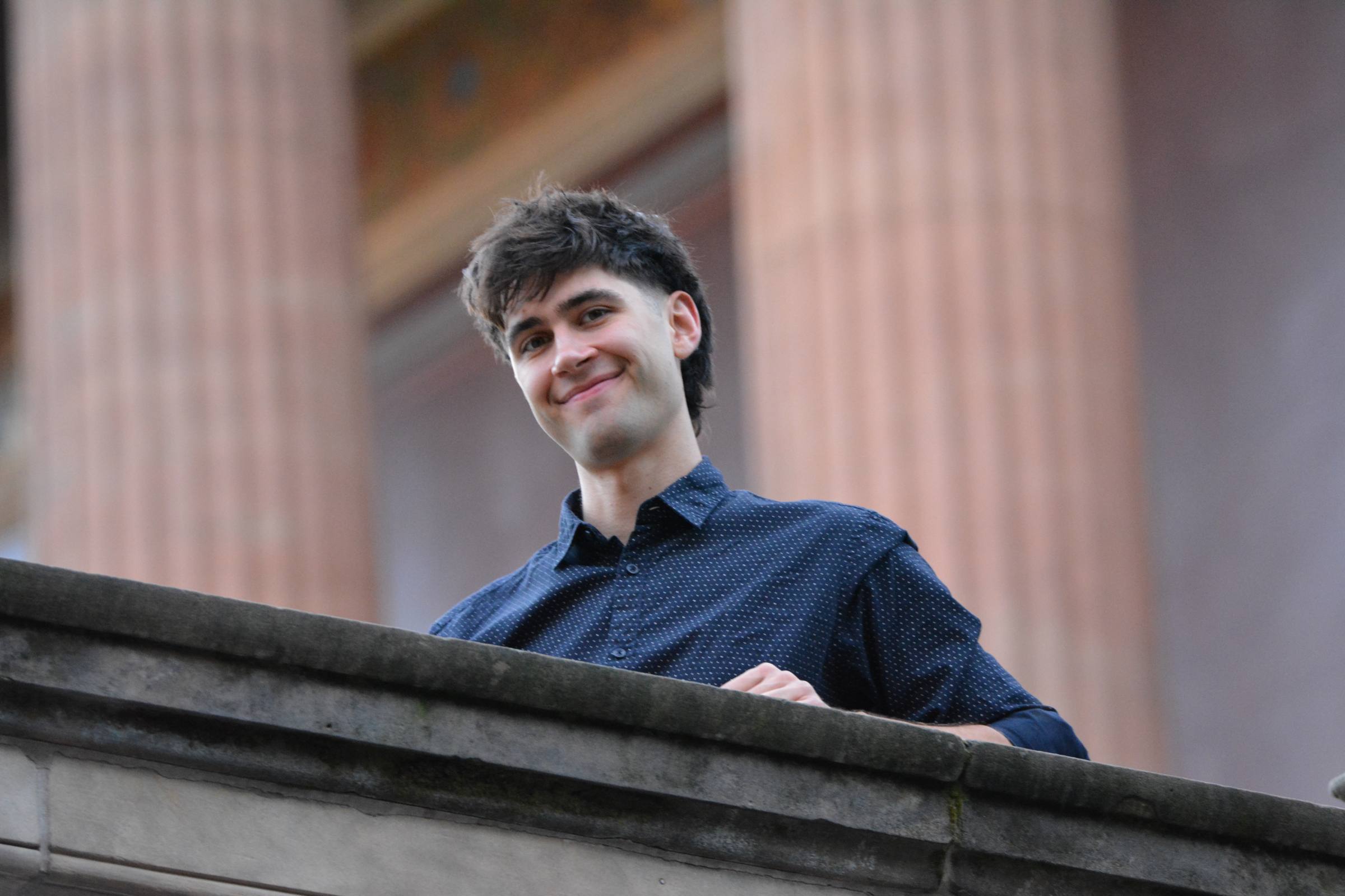 Lennert smiling down from a stone balustrade, red columns behind him